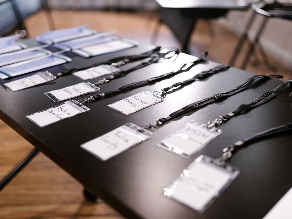 Name badges in clear holders with lanyards, laid out in rows on a table.
