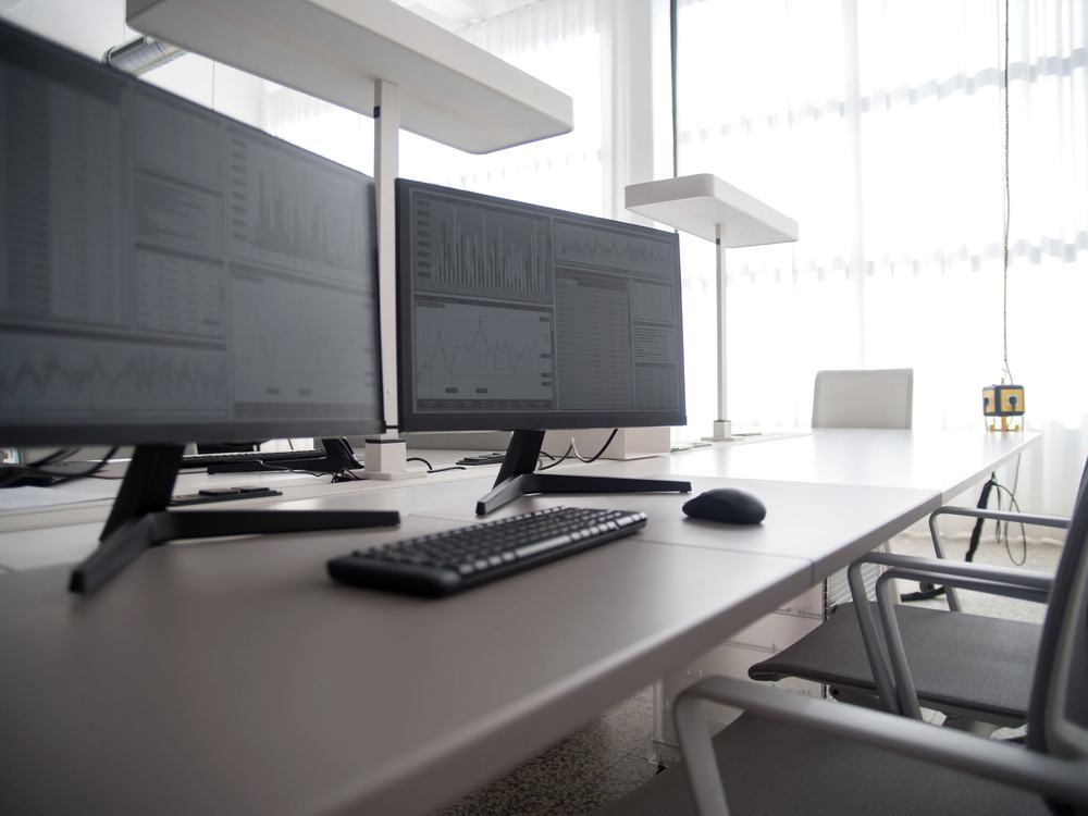 A row of desktop monitors and keyboards along a workstation bench in an office.