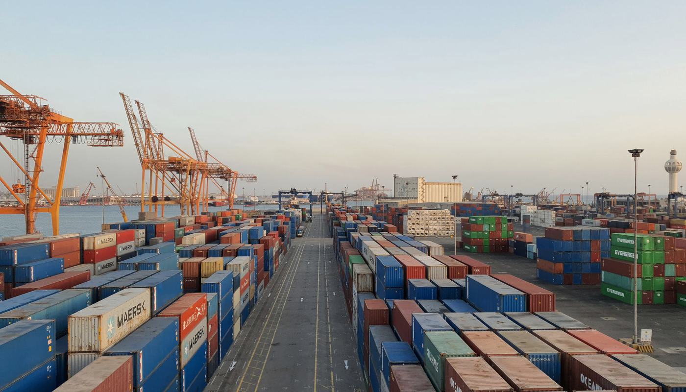 Rows of stacked shipping containers and gantry cranes at a container terminal.