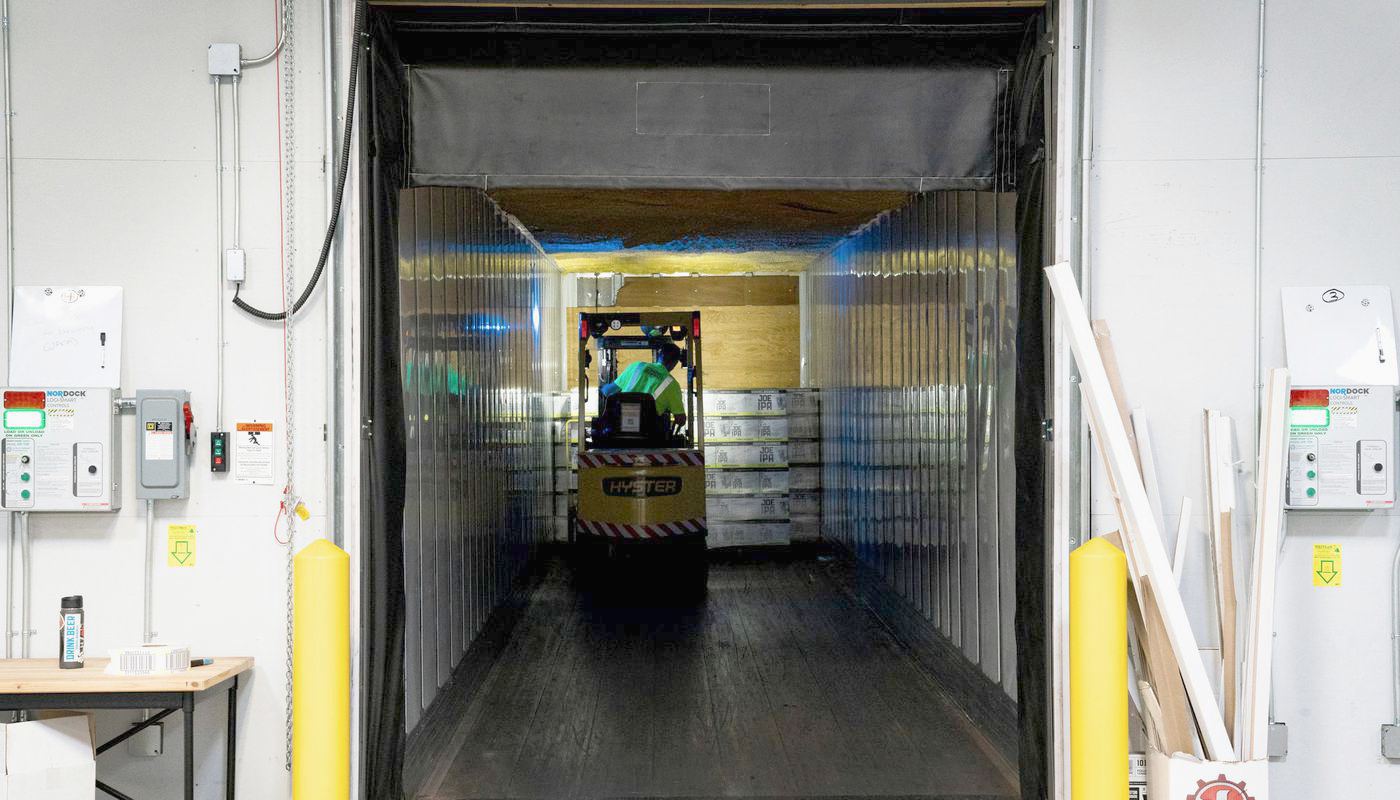 A warehouse loading dock bay with a trailer backed in and a forklift working inside.