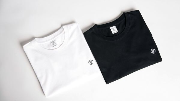 A folded white and a folded black t-shirt on a plain background.